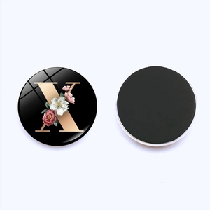 Detail of round crystal fridge magnet with letter X and floral design on white background