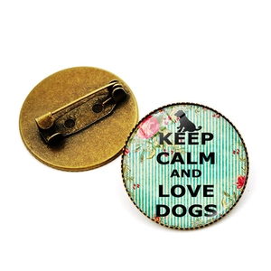 Ronde Keep Calm and Love Dogs speld met bronzen basis en bloemmotief onder een glazen koepel