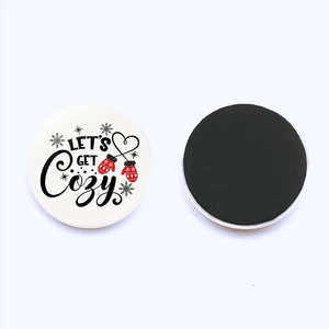 Detail of round Christmas fridge magnet featuring Let's Get Cozy text and black magnetic back