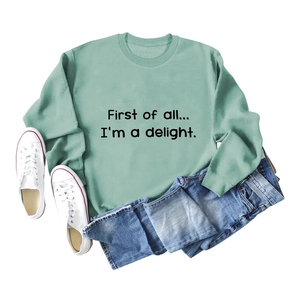 Flat lay of a light green crewneck sweatshirt with First of all text and blue denim jeans