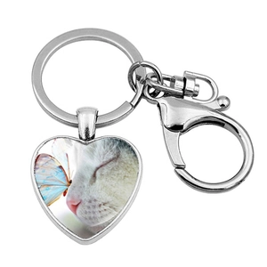 Detail of a heart-shaped silver keychain featuring a white cat and a blue butterfly