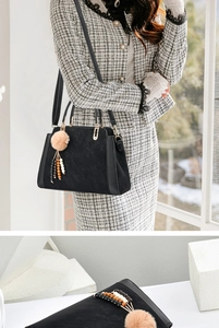 Détail du sac à main noir avec poignées dorées et breloque à pompon en peluche