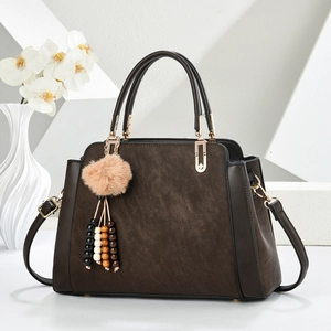 Sac à main en cuir marron foncé avec pompon en fourrure et bandoulière sur fond blanc