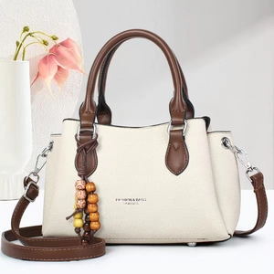 Detail view of beige crossbody bag with brown leather handles and wooden bead charm