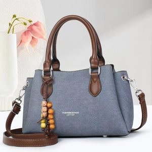 Detail of blue denim handbag featuring brown leather trim and colorful beaded tassel charm