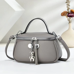 Grey pebbled leather handbag with bear pendant and detachable shoulder strap in studio light