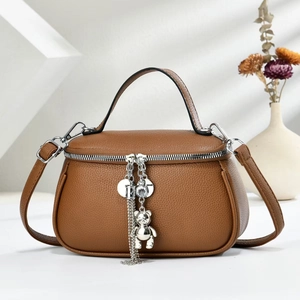 Detailed macro view of brown litchi pattern leather bag with silver bear charm tassel