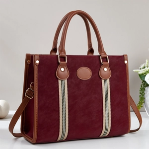 Detail view of burgundy tote bag featuring leather handles and decorative striped webbing
