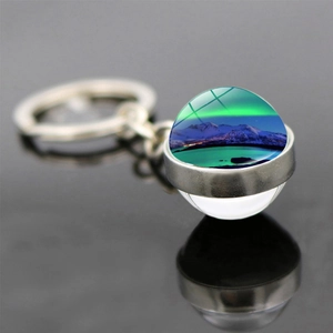 Macro shot of luminous aurora borealis glass ball keychain with snowy mountain view