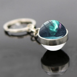 Macro shot of double-sided glass ball keychain with aurora borealis and forest scenery