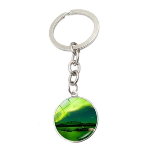 Close-up of circular silver keychain with bright green aurora borealis landscape glass dome