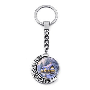 Détail du porte-clés de Noël rotatif avec pendentif maison enneigée dans un cadre lune