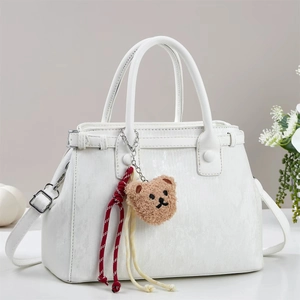 Détail d'un sac à main blanc texturé avec un joli pendentif ours en peluche marron