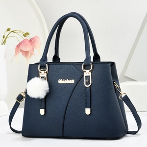 Minimalist navy blue leather handbag with gold hardware and plush charm on white stand