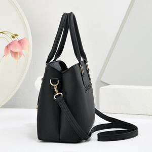 Side view of black lychee grain leather tote bag with gold hardware and white pompom