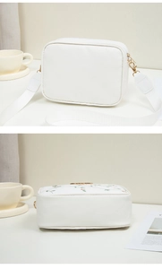Détail de la broderie florale et du logo doré sur le sac à bandoulière blanc