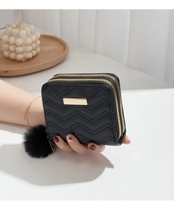 Détail du portefeuille noir matelassé avec double fermeture éclair et pompon en peluche