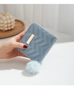 Détail d'un portefeuille bleu clair à coutures ondulées avec pompon et accents dorés