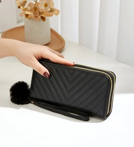 Detail of black double zipper quilted wallet with decorative pompom and wrist strap
