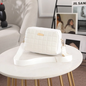 Sac bandoulière matelassé blanc avec détails dorés et large sangle sur table en marbre