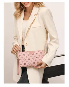 Pink crossbody bag with clover patterns and golden chain strap shown on a cream blazer