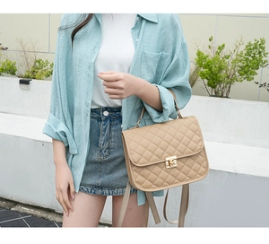 Quilted beige handbag featuring a gold metal lock and top handle in outdoor lighting