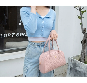 Détail du sac à main matelassé rose avec ornement abeille dorée porté par un modèle