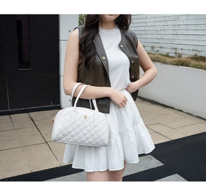 Détail d'un sac à main matelassé blanc avec emblème de camélia doré et couture