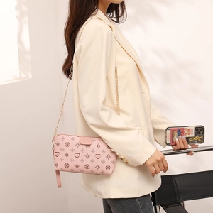Pink crossbody bag with heart pattern print and gold chain strap worn by model