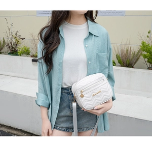 Outdoor shot of a white V-quilted crossbody bag with a gold metal logo and slim shoulder strap