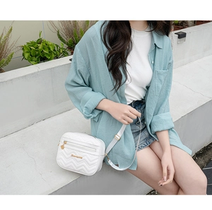 Close-up of white V-quilted shoulder bag with gold hardware worn by a model