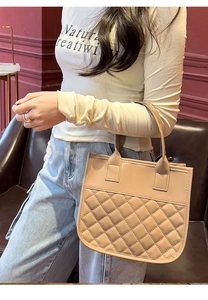 Detailed view of beige quilted handbag with wide handle held in a retro setting