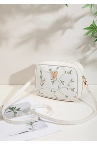 Detail of floral embroidery and gold butterfly ornament on white crossbody camera bag