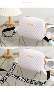 Detail of white V-quilted crossbody bag featuring gold hardware and lettered woven strap
