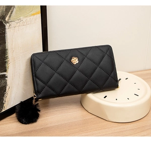 Detail of black quilted long wallet with golden flower logo and fluffy pompom charm