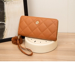 Detail of caramel quilted long wallet with golden flower hardware and fuzzy ball charm
