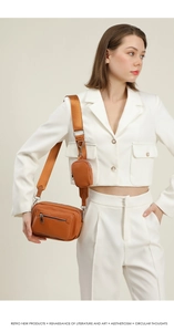 Detail of a brown leather crossbody bag with a round coin pouch on a wide woven strap