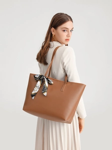 Close-up of brown tote bag with premium leather texture and decorative silk scarf accessory