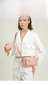 Pink crossbody bag with detachable pouch and wide fabric strap on a white formal suit