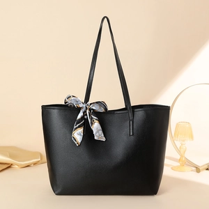 Minimalist black leather tote bag with printed silk scarf on a warm studio background