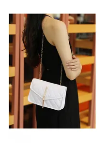 Detail of white quilted crossbody bag with gold chain and metal tassel on a model