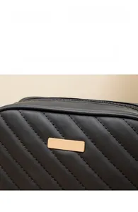 Detail einer gesteppten schwarzen Ledertasche mit polierter goldener Logoplakette