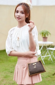 Outdoor view of a model wearing a brown quilted crossbody bag with a deer charm and chain strap