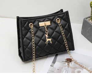 Detail of black quilted leather texture with golden deer pendant and chain strap