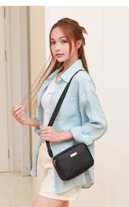 Detail of black quilted crossbody bag with golden hardware and wide fabric strap
