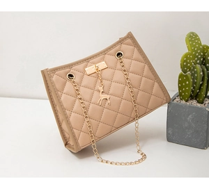 Detail of beige quilted shoulder bag featuring gold chain and a metal deer charm pendant
