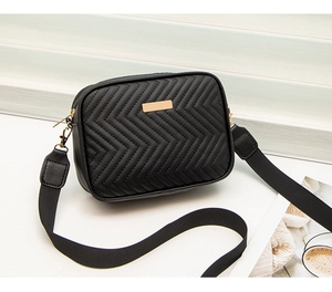 Detail view of black quilted camera bag with gold hardware and wide textile strap