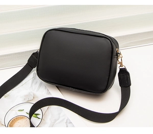 Flat lay of black embroidered crossbody bag with gold hardware and wide woven strap