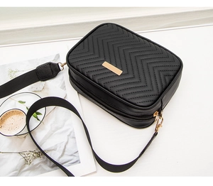 Detail of black chevron quilted camera bag with golden hardware and wide strap