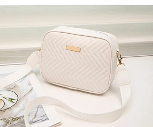 Detail of white chevron quilted crossbody bag with gold hardware and wide canvas strap